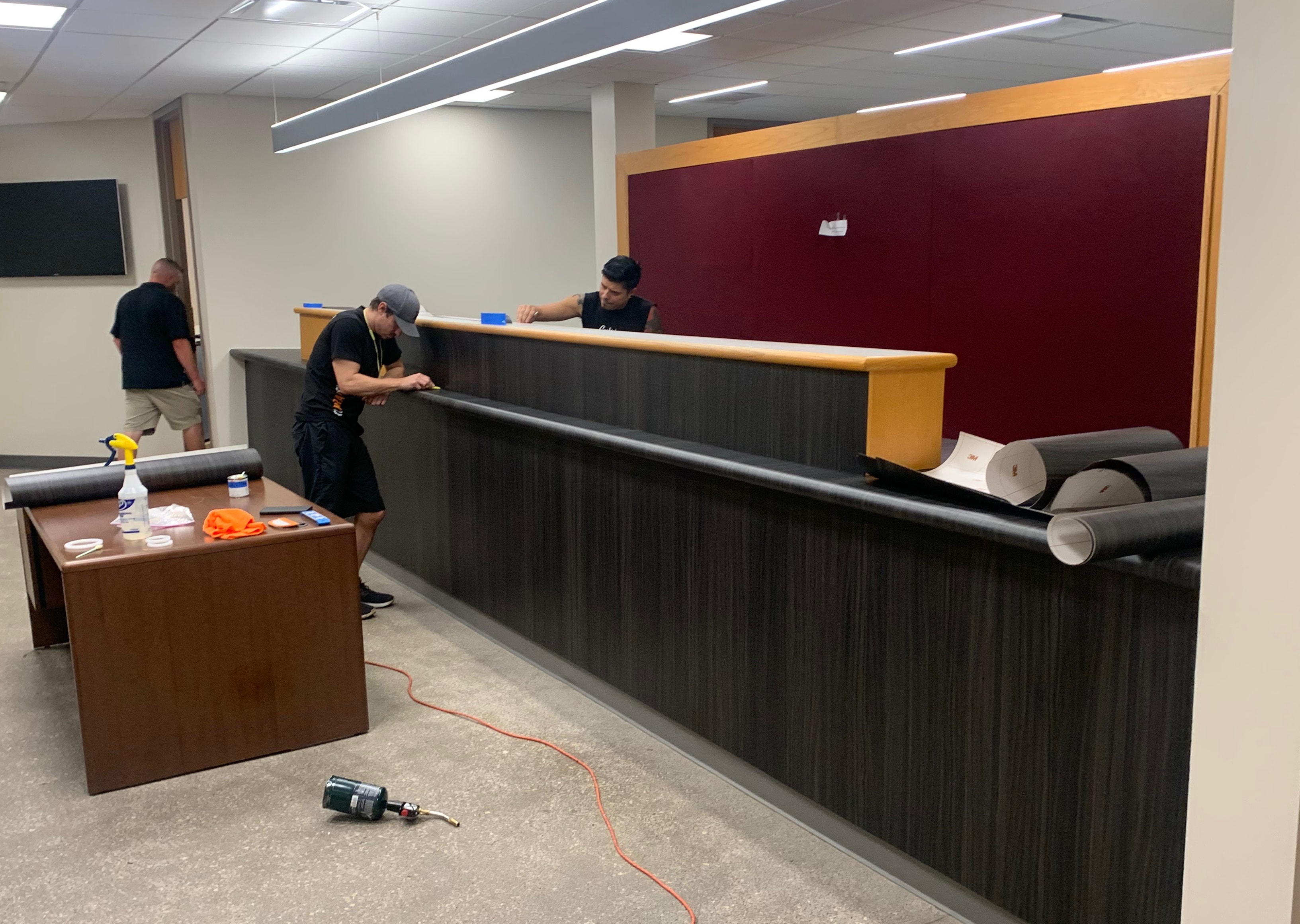 Architectural Wraps crew installing dark wood grain vinyl surface wrap on commercial reception counter