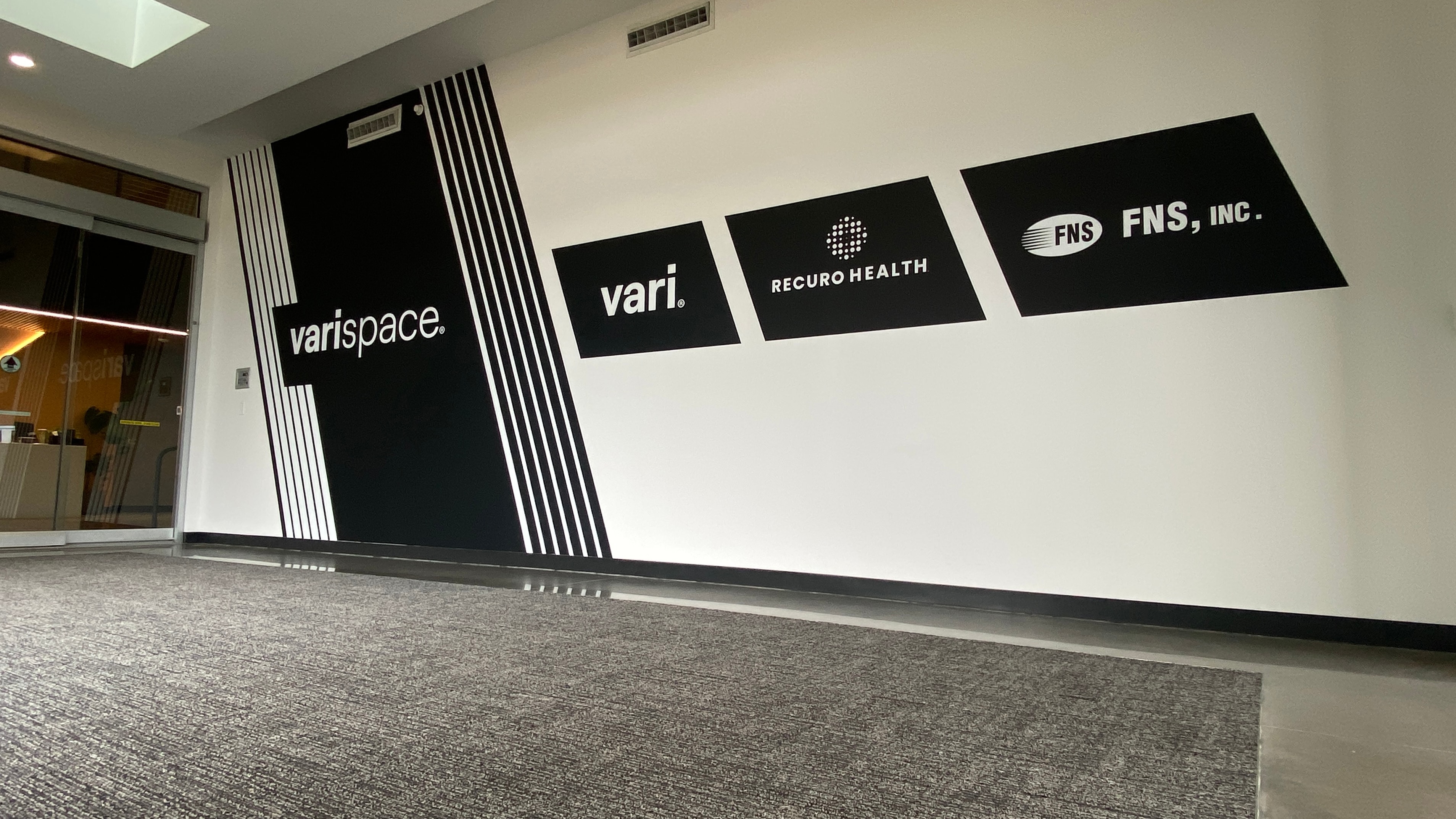 Varispace office lobby client logo wall wrap featuring Vari, Recuro Health and FNS Inc branding by Architectural Wraps